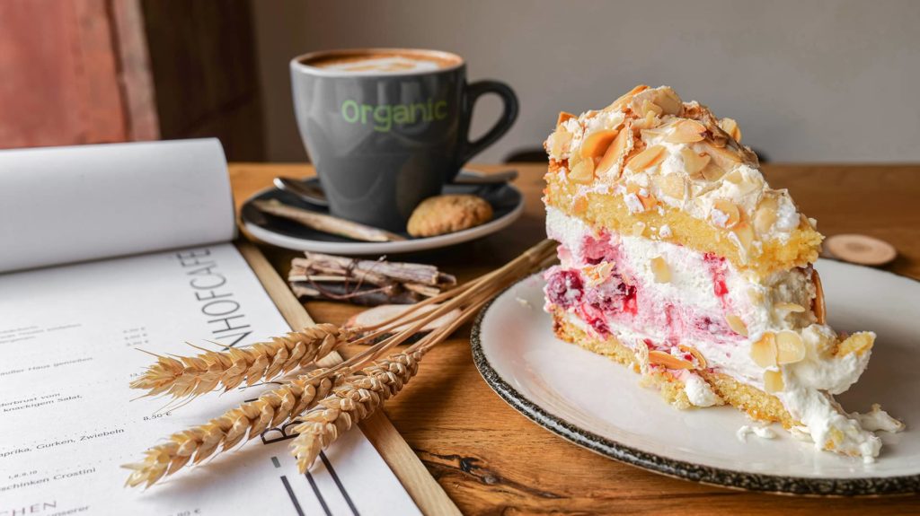 Stück Kuchen und ein Cappuccino und Kerze auf Holztisch im Café