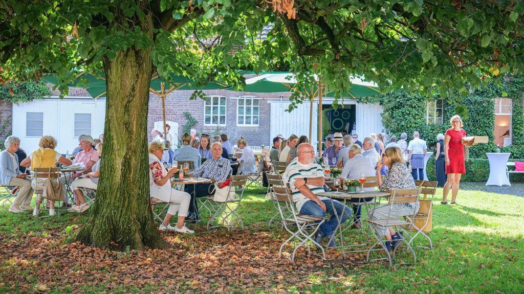 Menschen sitzen an Tischen unter einem Baum