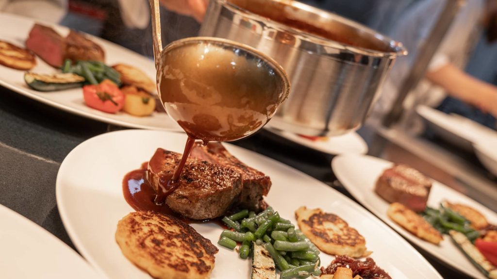 Koch schüttet Sauce auf Teller mit Steak