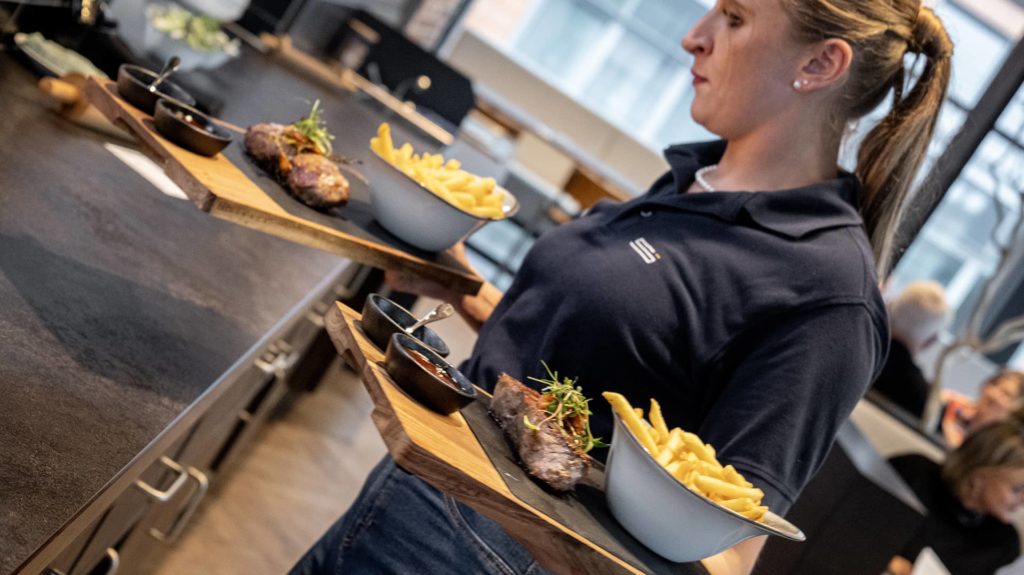 Servicemitarbeiterin trägt Steak und Pommes auf Schieferplatten