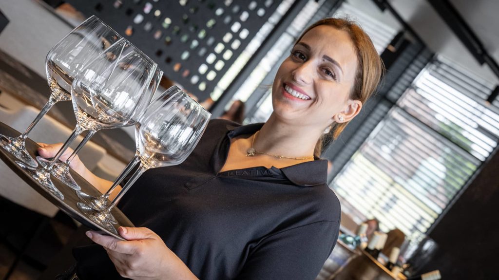 Servicemitarbeiterin lächelt mit Tablett voller Gläser